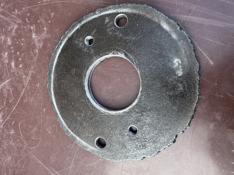 Circular metal flange with four bolt holes and rough edge.
