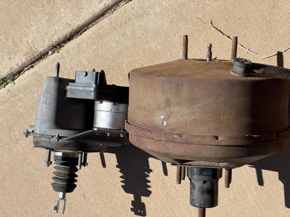Two brake boosters, one modern gray and one old rusty, on a concrete surface.