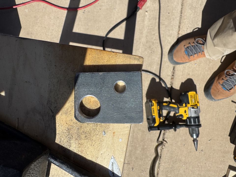Metal bracket with two holes and a power drill on a wooden surface.