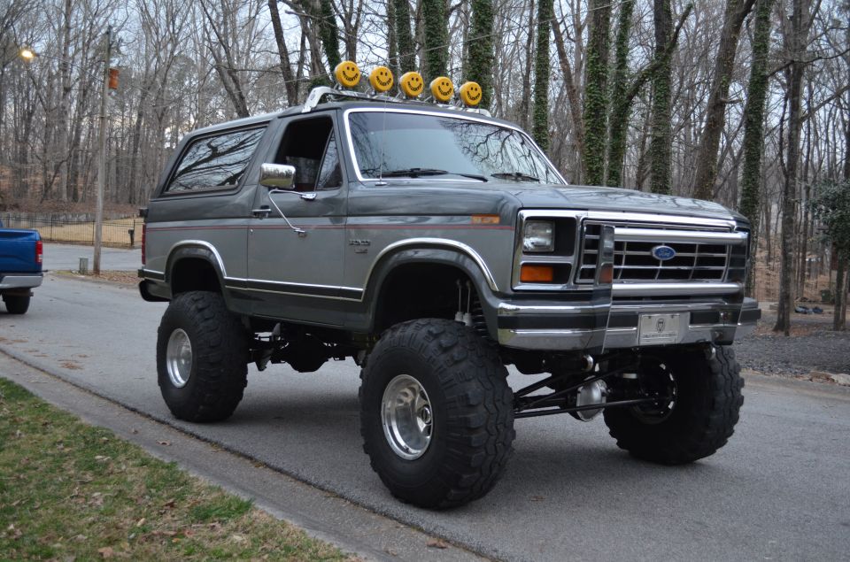 Lifted gray 1980s Ford Bronco with smiley face light bar.