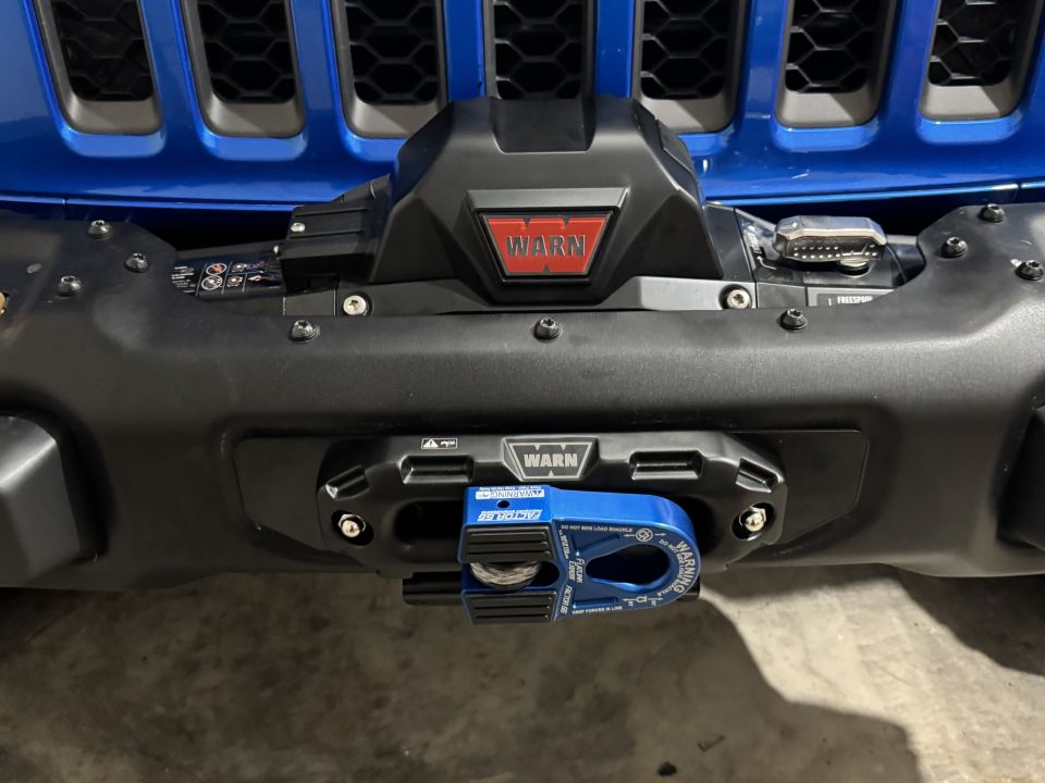 Blue Jeep Wrangler front bumper with a black Warn winch and blue Warn winch hook.