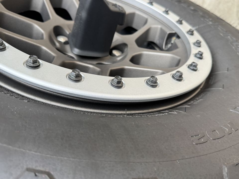 Close-up of a tire and wheel with beadlock ring and lug nuts.