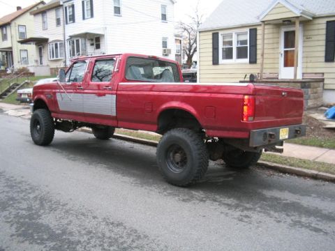 1979 Ford Bronco - This lifted, red crew cab pickup truck features distinctive silver trim along its side panels.
