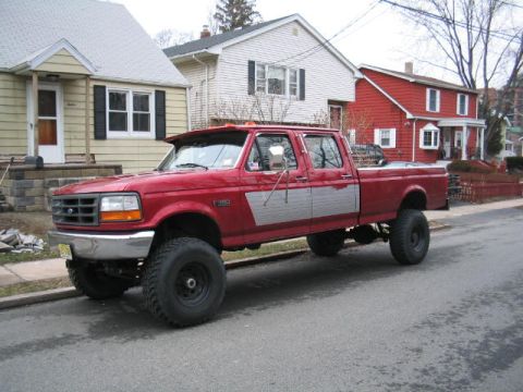 1979 Ford Bronco - This red pickup truck has a crew cab and large tires, with silver paneling on the side.
