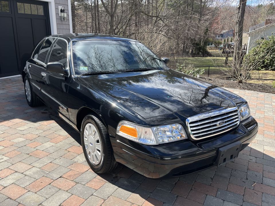 Black Ford Crown Victoria sedan, front three-quarter passenger-side view on driveway