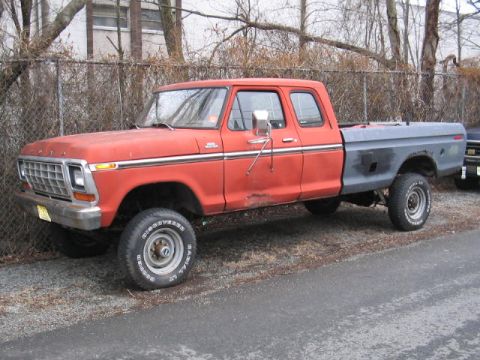 1979 Ford Bronco - This red Ford F-Series pickup truck has a grey bed and is parked on a gravel surface.