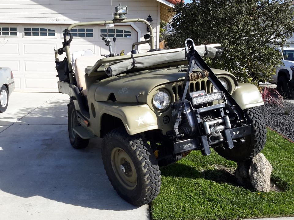 Modified olive drab Jeep M38A1 with winch and light bar parked on a driveway.
