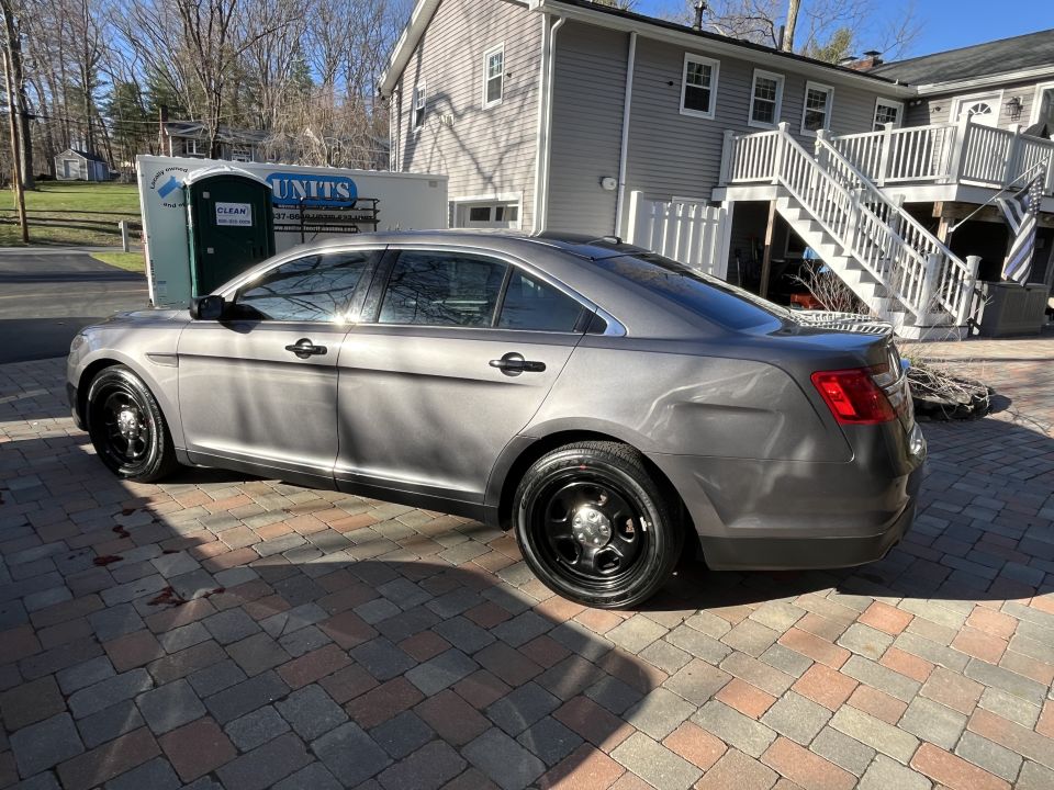 Gray Ford Taurus Police Interceptor sedan, rear three-quarter view, parked on paver driveway
