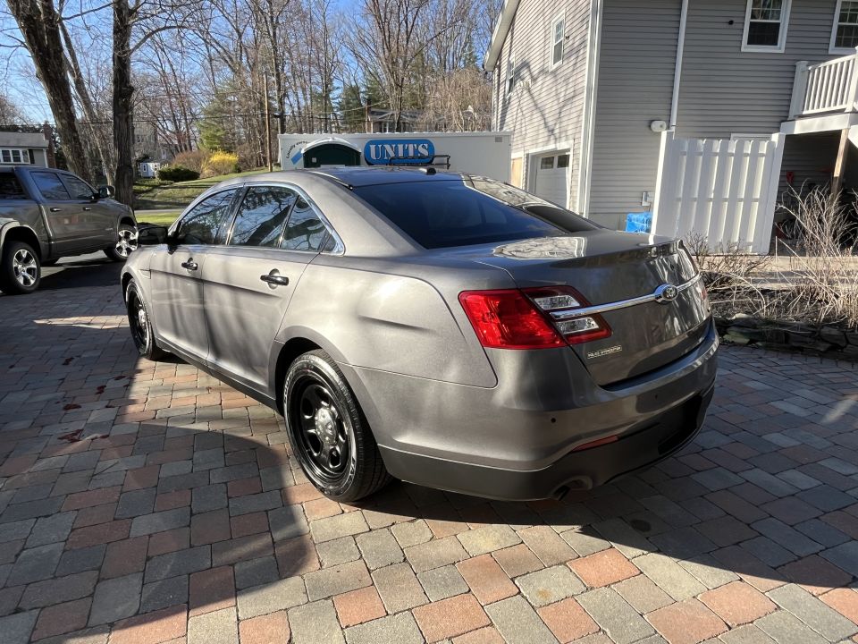 Gray Ford Taurus sedan, rear three-quarter view, parked in driveway by house