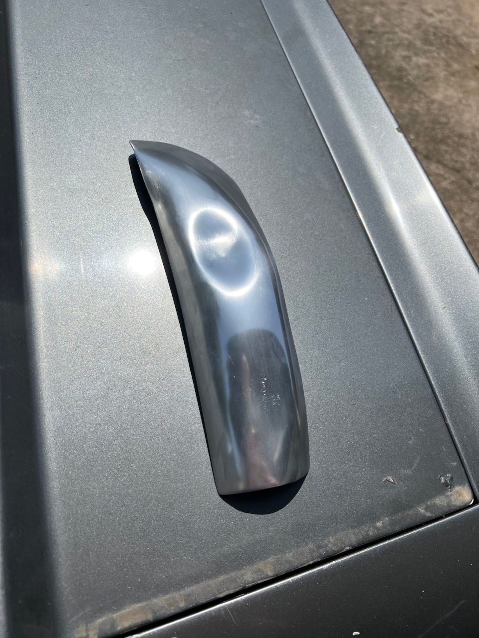 Chrome trim piece with a curved shape resting on a gray car hood