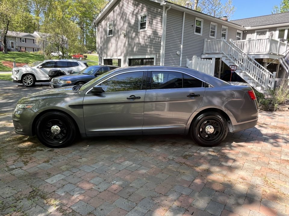 Gray Ford sedan with black steel wheels parked on a brick driveway. Another SUV and a dark sedan are behind it