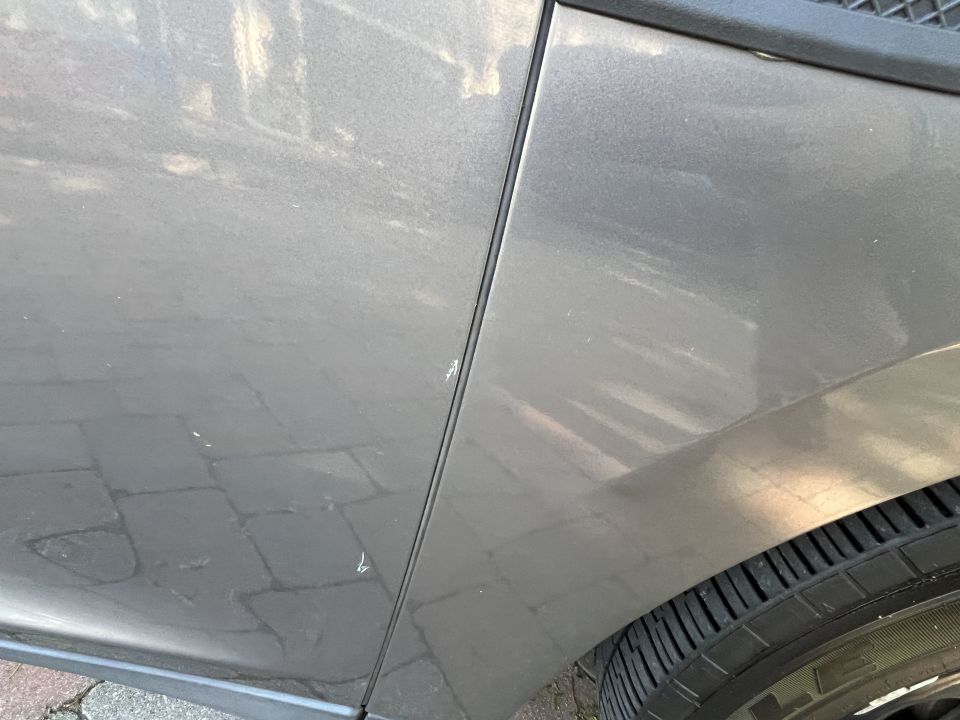 Close-up of a gray car door panel showing scratches and a portion of the tire