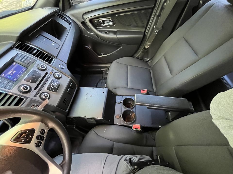 Interior of a police car showing the center console with equipment, cup holders, and seats