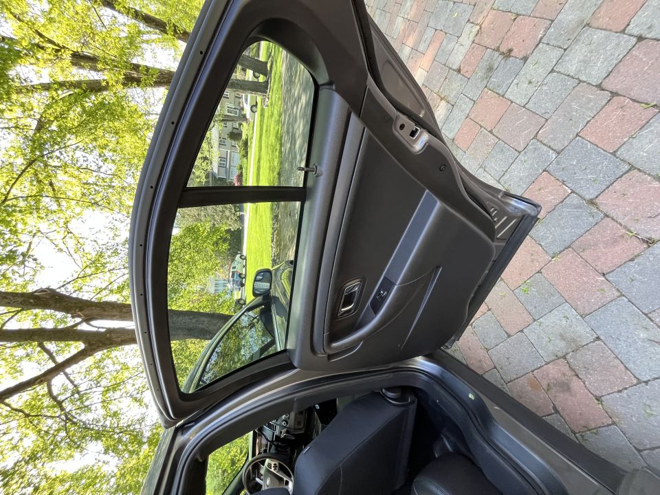View of a car's interior and open front door, looking out at a tree-lined street with houses