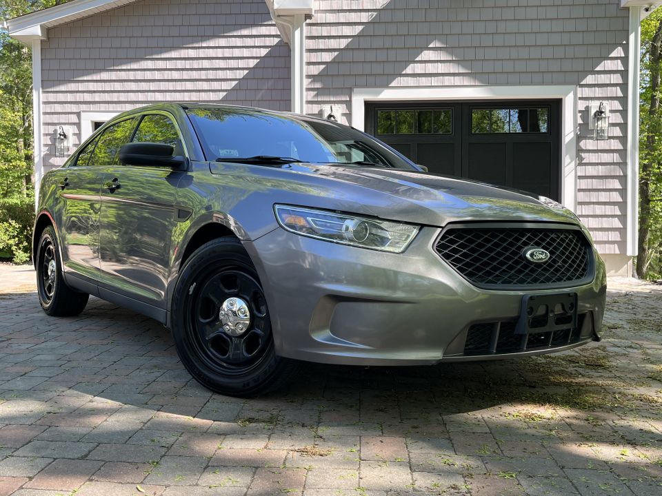Gray Ford sedan with black steel wheels parked in front of a garage