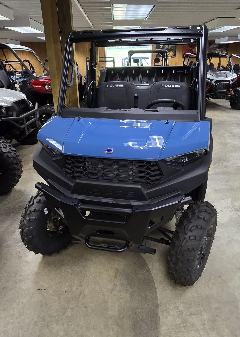Blue Polaris side-by-side utility vehicle parked indoors with other vehicles visible