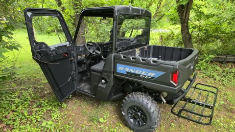 2025 Polaris RANGER - A black Polaris Ranger side-by-side vehicle is parked outdoors with its driver's side door open, revealing the interior and cargo bed.