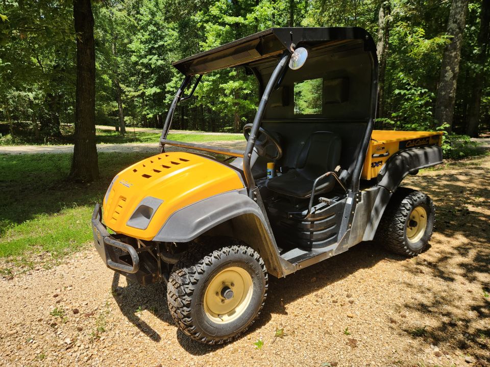 Yellow utility vehicle with black roof and seats, parked on a gravel path in a wooded area