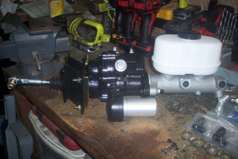 1978 Ford Bronco - A brake booster and master cylinder assembly sits on a workbench, surrounded by tools and parts.