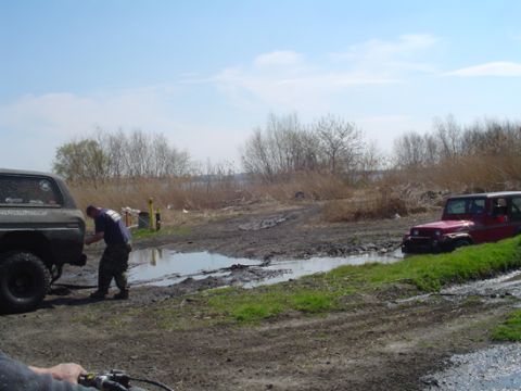 1979 Ford Bronco - Two off-road vehicles are stuck in mud, with one person attempting to work on the dark SUV.