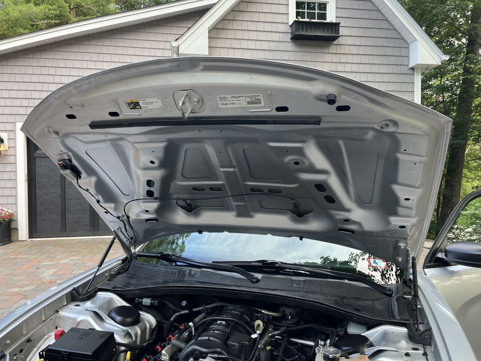 Underside of a raised silver vehicle hood over the engine bay