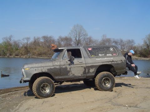 1979 Ford Bronco - A muddy 1978 Ford Bronco sits by the water, with a person perched on its rear bumper.