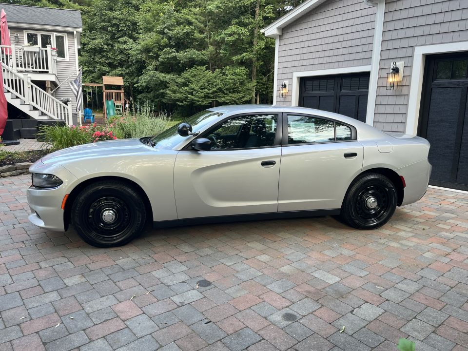Silver sedan parked on a brick driveway in front of a garage. It has black steel wheels and a police-style light on the driver's side mirror