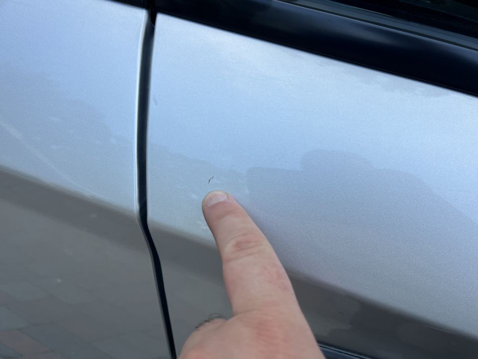 Finger pointing to a small paint chip on a silver car door panel