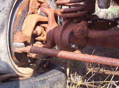 1988 Ford Bronco - Close-up of heavily rusted vehicle suspension parts, including a coil spring and tie rod end.