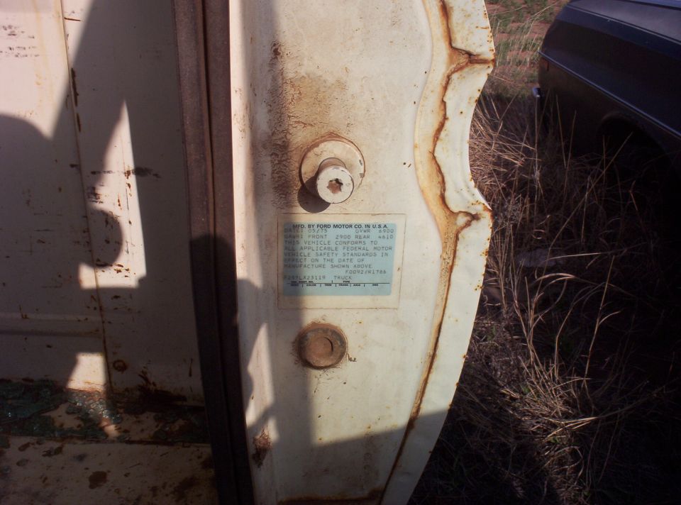 Ford certification label on a weathered white truck door edge beside the latch striker