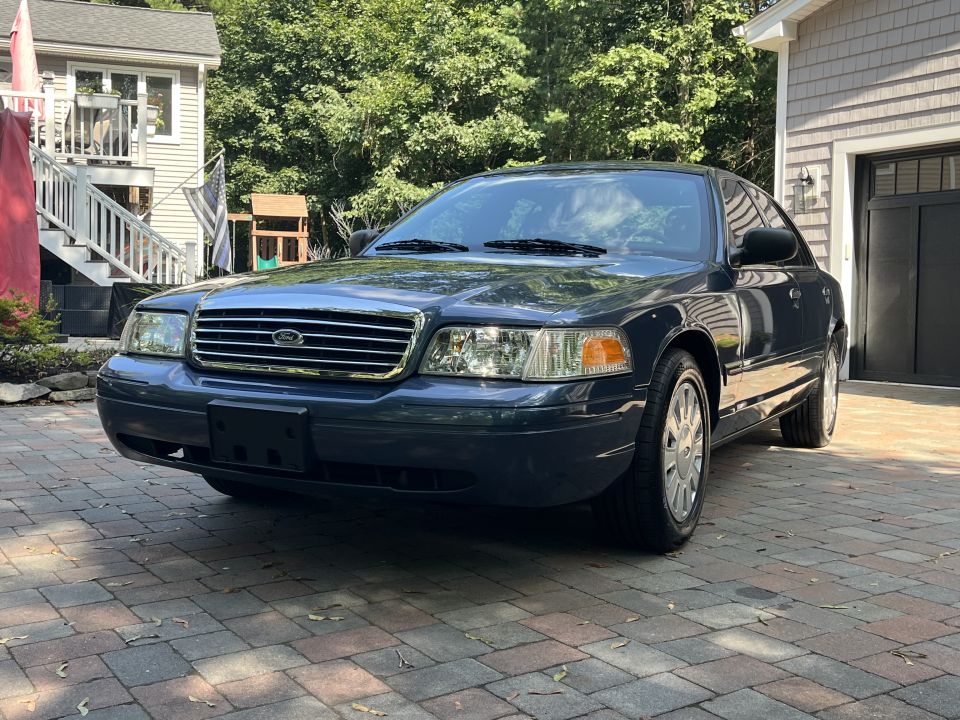 Blue Ford Crown Victoria sedan front three-quarter view parked on paver driveway