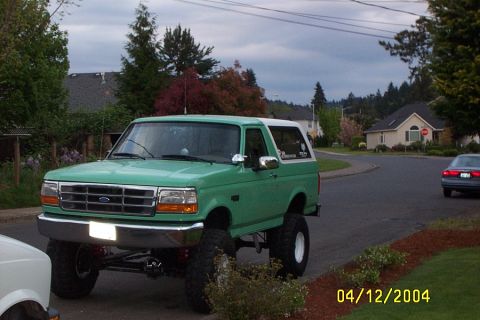 1996 Ford Bronco - A lifted green 1992 Ford Bronco with a white top is parked on a street, with another car in the background.