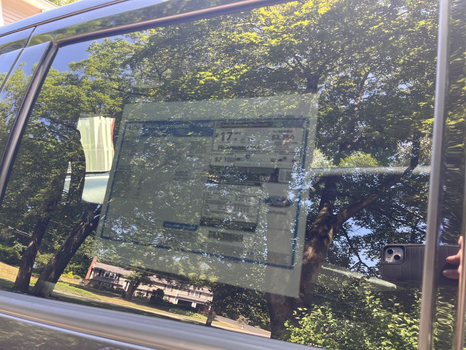 Monroney window sticker inside a vehicle rear window, mostly obscured by glare