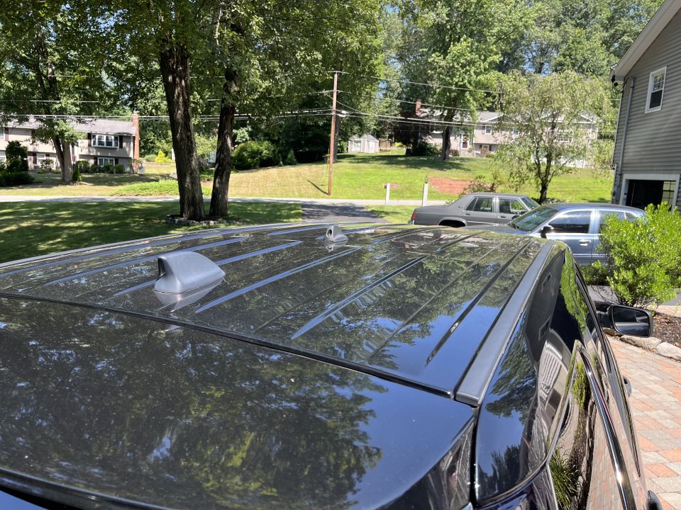 Roof and rear antenna of black Ford Explorer with neighborhood in background