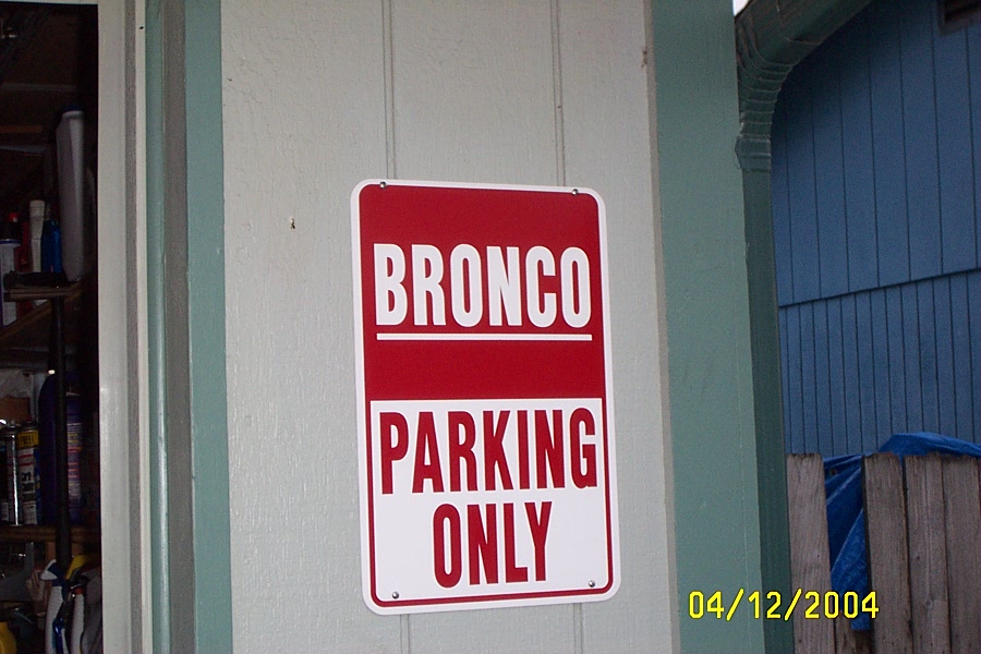 Red and white Bronco Parking Only sign mounted on a cream wall beside a garage doorway