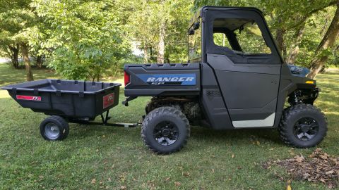2025 Polaris RANGER - A dark-colored utility vehicle, identified as a RANGER, is shown hitched to a trailer in a grassy outdoor setting.