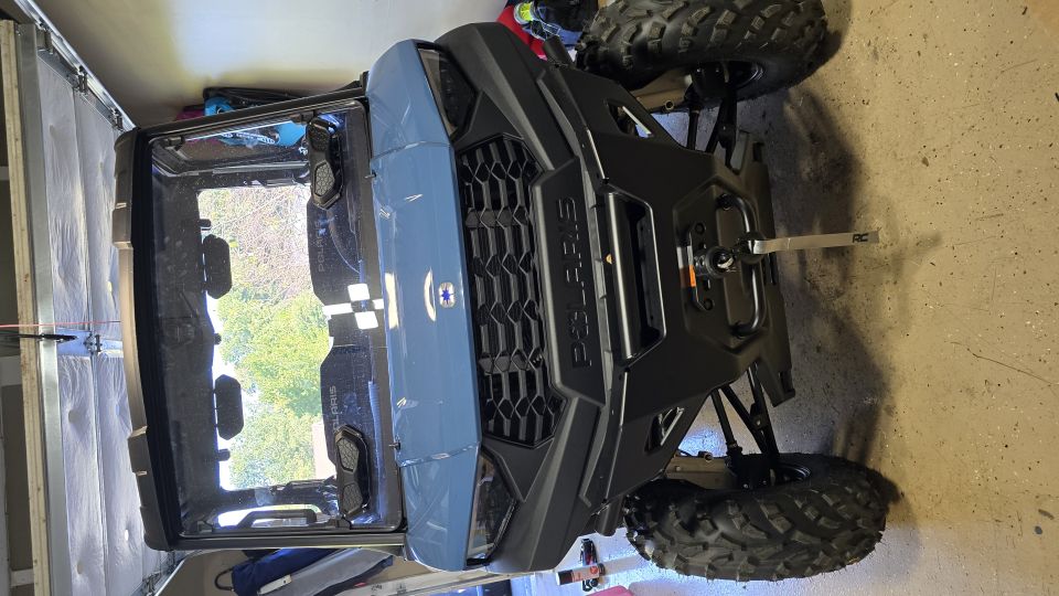 Front of slate blue Polaris UTV with POLARIS grille, winch, and off-road tires in a garage