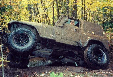 1995 Ford Bronco - Jeep Wrangler TJ navigating muddy off-road terrain during daytime.