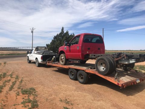 2008 Ford F-250 - A red 2008 Ford F-250 chassis is transported on a trailer towed by a white pickup truck.