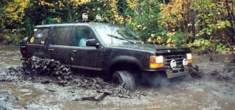 1995 Ford Bronco - A black Ford Explorer navigates a muddy trail with trees in the background.