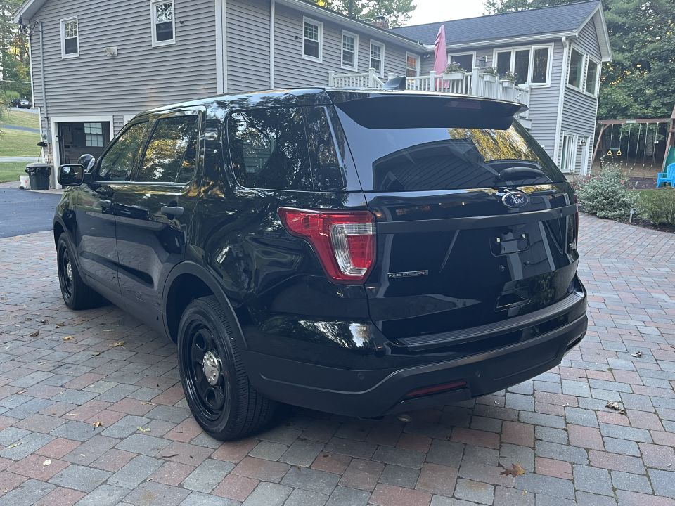 Black Ford Explorer SUV parked on a brick driveway, rear view. Police equipment visible