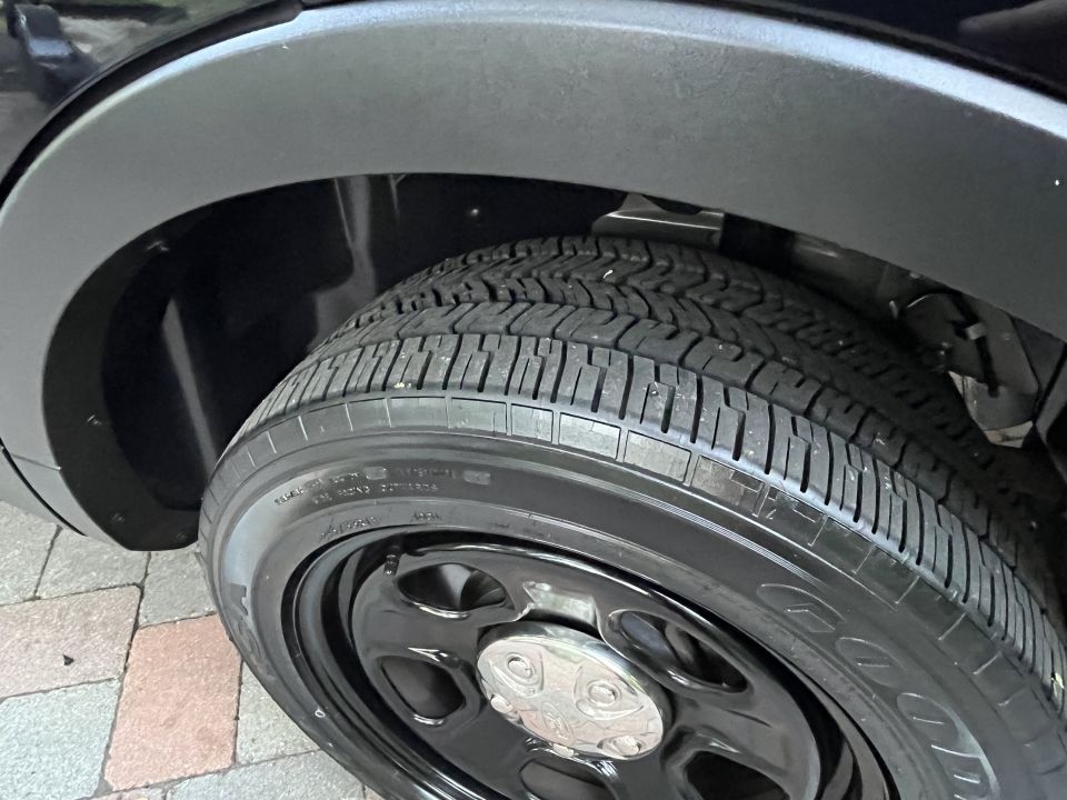 Close-up of a black vehicle's rear wheel well and tire with a steel wheel