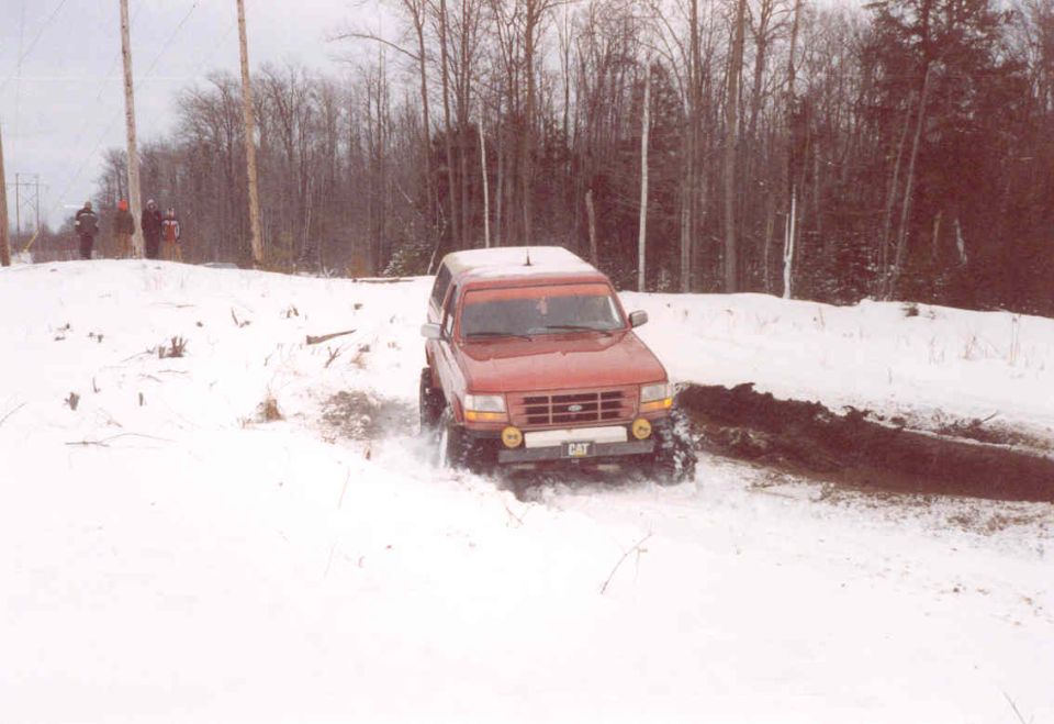1995 Ford Bronco driving through snow with CAT logo on front bumper