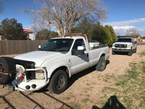 2005 Ford F-250 - A white pickup truck is parked outside with a spare tire mounted on its front bumper. Another truck is visible in the background.