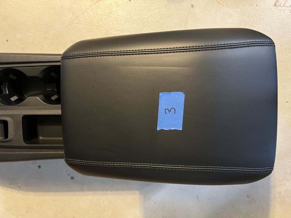 Black leather center console armrest with blue tape labeled '3' and cupholder assembly