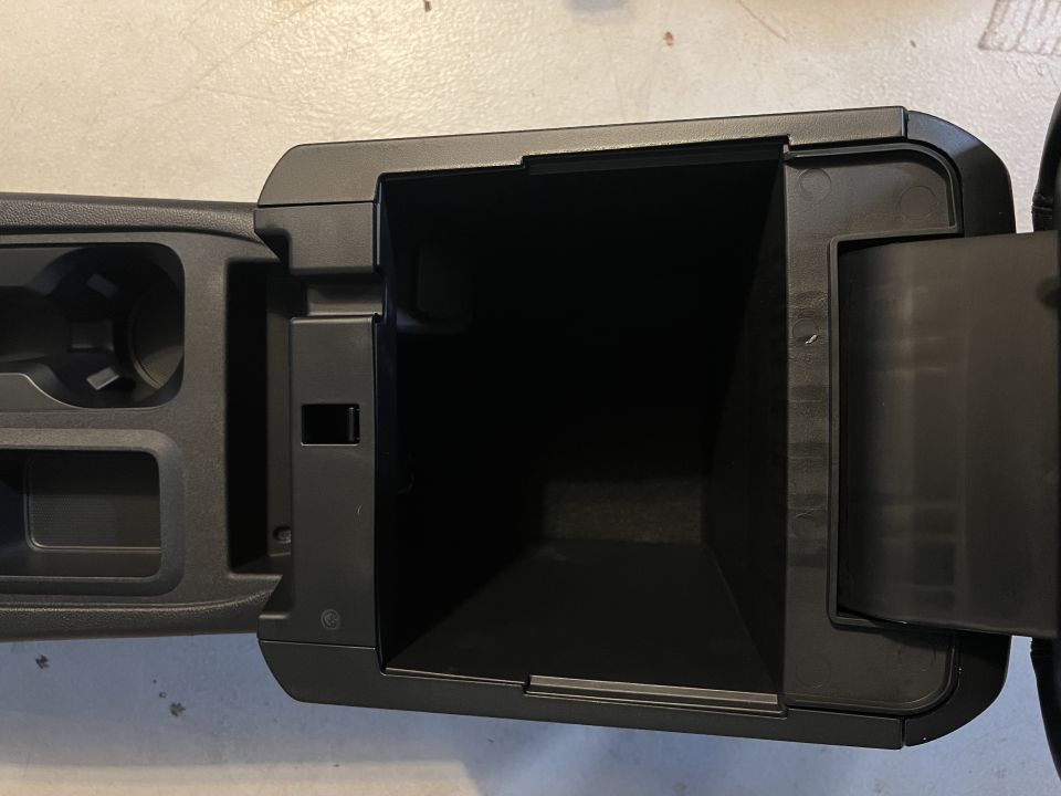 Black open center console storage compartment with cupholders visible to the left