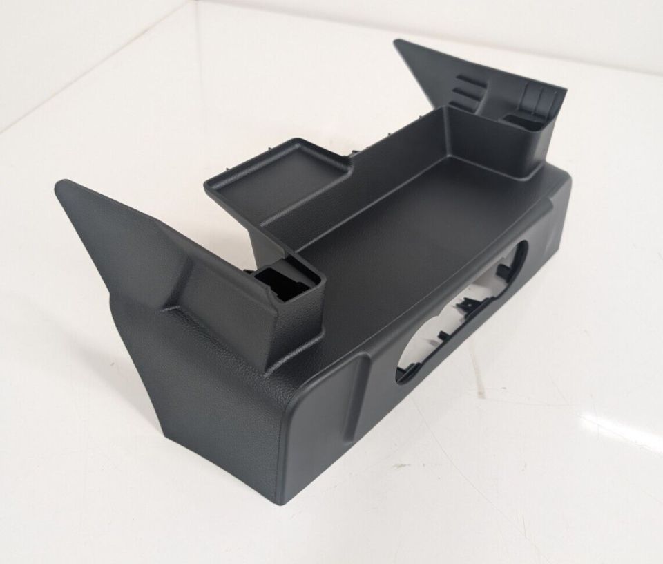 Black plastic center console trim piece with various compartments and cutouts