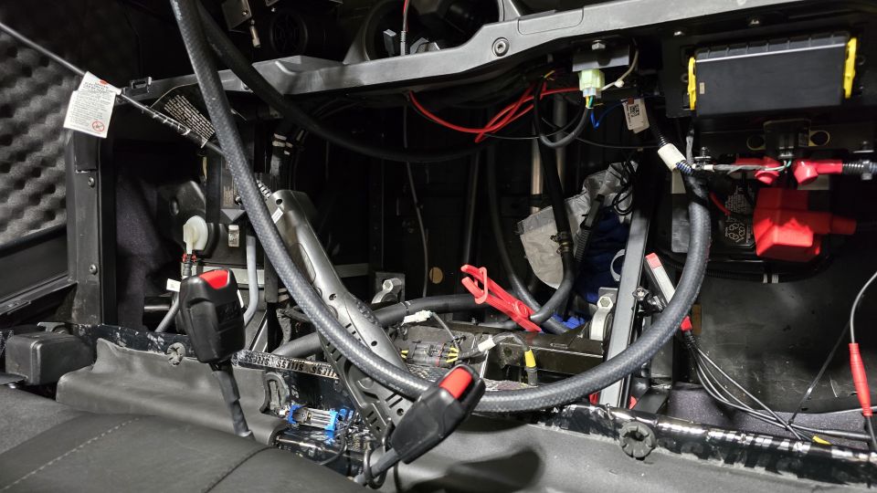 Vehicle interior with complex wiring, battery, and seatbelt buckle visible