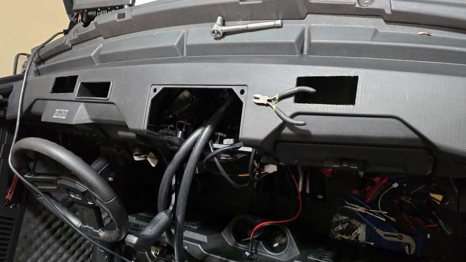 UTV dashboard with open compartments showing wiring, steering wheel, and tools