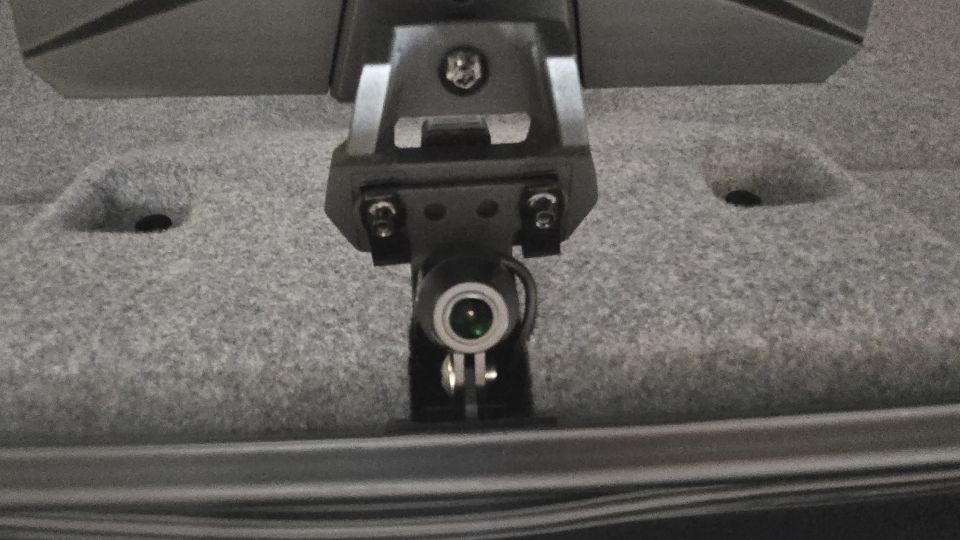 Dash cam mount attached to gray carpeted surface, with a small camera lens visible